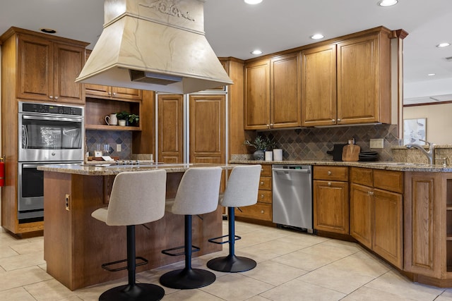 kitchen with light stone counters, stainless steel double oven, sink, and custom exhaust hood