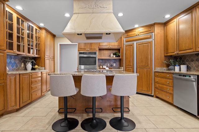 kitchen with light tile patterned flooring, appliances with stainless steel finishes, island range hood, a center island, and light stone countertops