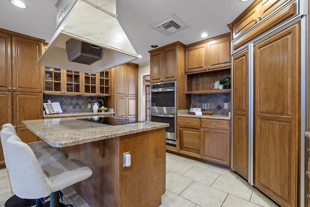 kitchen with island range hood, double oven, a center island, light stone countertops, and black electric cooktop