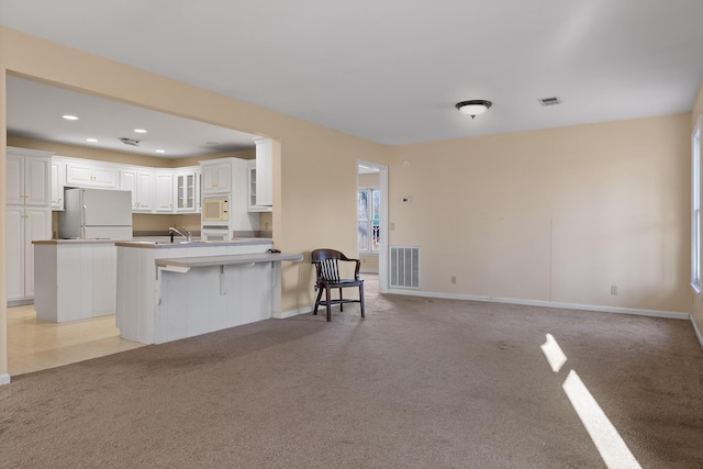 kitchen with a kitchen bar, white cabinetry, a center island, light colored carpet, and white appliances