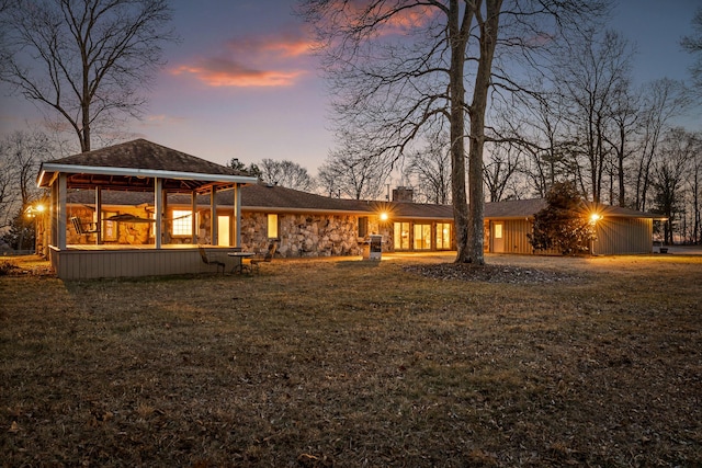 back house at dusk featuring a lawn