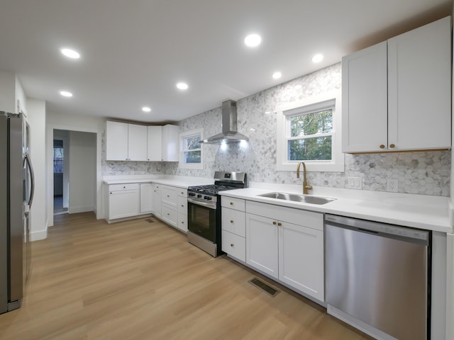 kitchen with sink, white cabinetry, light hardwood / wood-style floors, wall chimney range hood, and appliances with stainless steel finishes