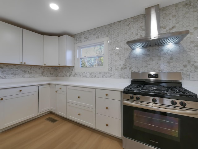 kitchen with decorative backsplash, stainless steel range with gas cooktop, white cabinetry, and wall chimney exhaust hood