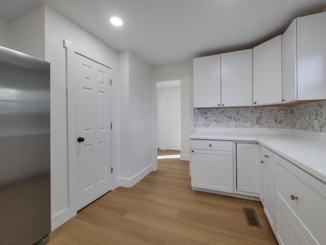 kitchen with light hardwood / wood-style flooring, white cabinetry, decorative backsplash, and stainless steel refrigerator