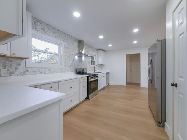 kitchen featuring stainless steel appliances, white cabinetry, light hardwood / wood-style floors, decorative backsplash, and wall chimney range hood