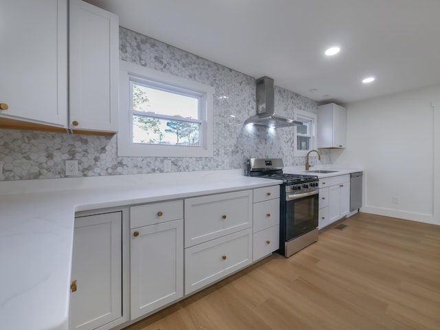 kitchen with appliances with stainless steel finishes, white cabinets, wall chimney range hood, and sink