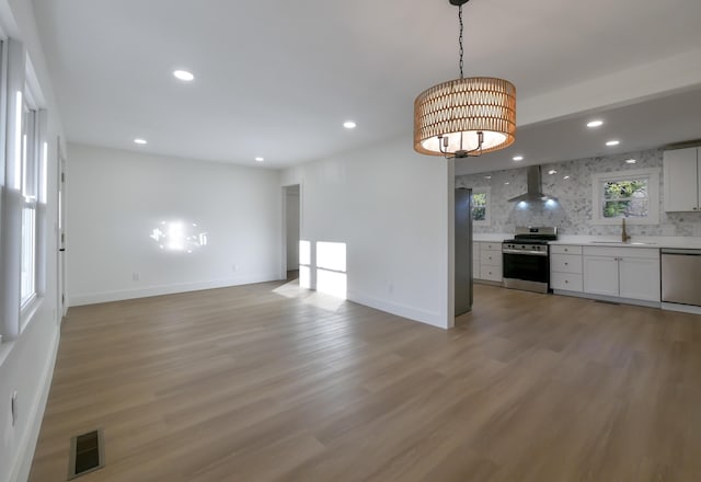 kitchen with wall chimney exhaust hood, decorative backsplash, white cabinets, appliances with stainless steel finishes, and sink