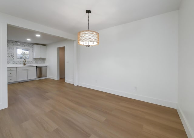 interior space with dishwasher, hanging light fixtures, light wood-type flooring, sink, and white cabinetry