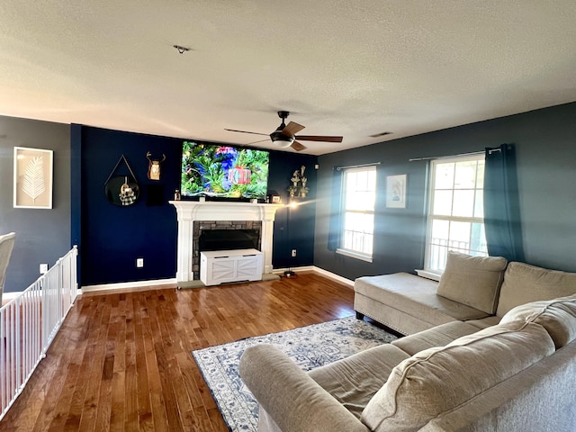 unfurnished living room featuring a fireplace, wood-type flooring, a textured ceiling, and ceiling fan