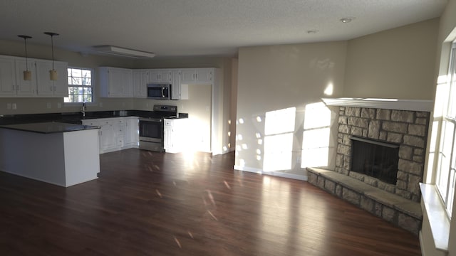 kitchen featuring a textured ceiling, hanging light fixtures, stainless steel appliances, white cabinets, and a fireplace