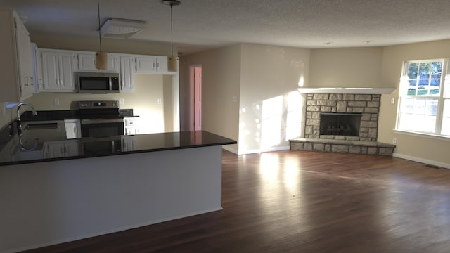 kitchen featuring hanging light fixtures, electric range oven, white cabinetry, a fireplace, and sink