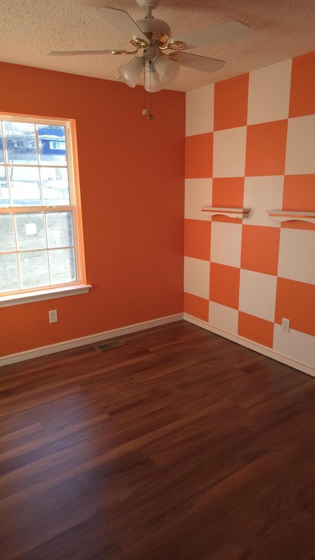 empty room featuring ceiling fan, dark wood-type flooring, and a textured ceiling