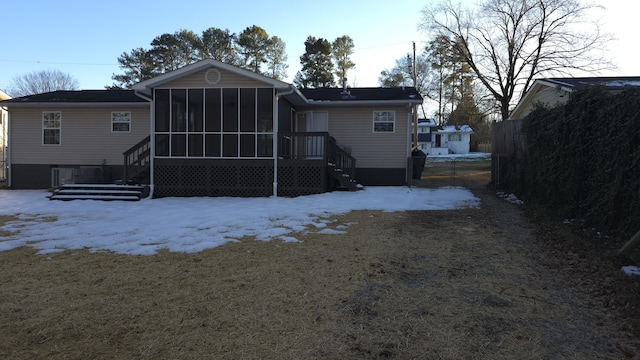 snow covered rear of property featuring a sunroom