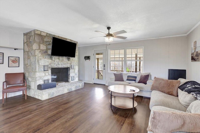 living room with a stone fireplace, dark hardwood / wood-style flooring, ornamental molding, ceiling fan, and a textured ceiling