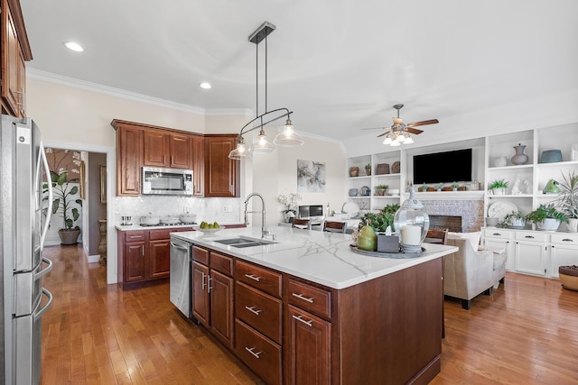 kitchen featuring sink, hanging light fixtures, an island with sink, a fireplace, and appliances with stainless steel finishes