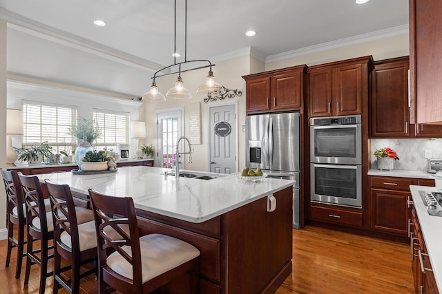 kitchen featuring pendant lighting, a breakfast bar, a center island with sink, sink, and appliances with stainless steel finishes