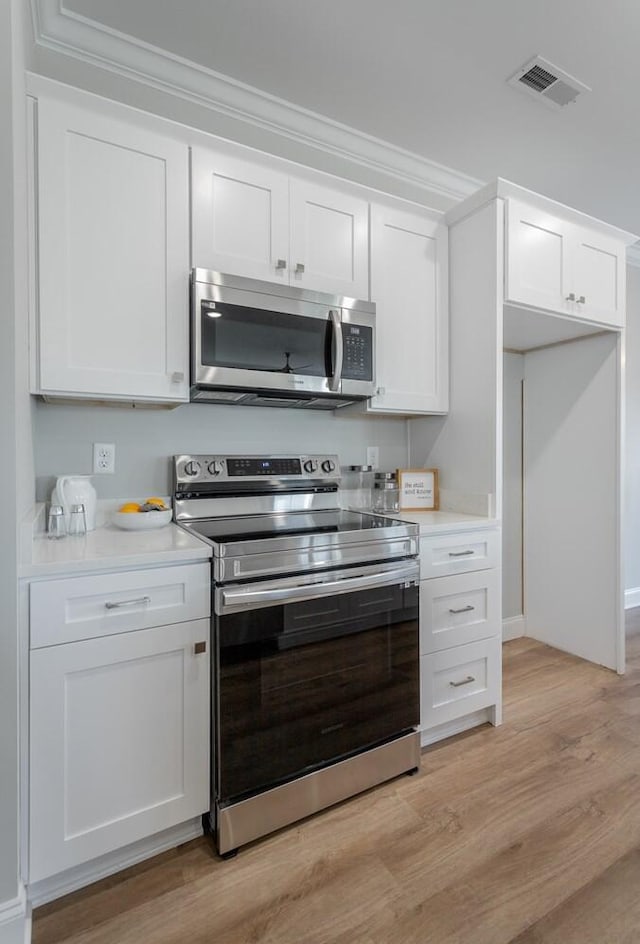 kitchen with light hardwood / wood-style flooring, white cabinets, ornamental molding, and appliances with stainless steel finishes