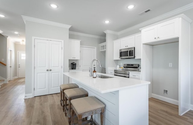 kitchen featuring white cabinetry, stainless steel appliances, crown molding, an island with sink, and a breakfast bar area