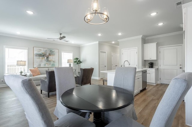 dining room with a healthy amount of sunlight, light hardwood / wood-style floors, ceiling fan with notable chandelier, and ornamental molding