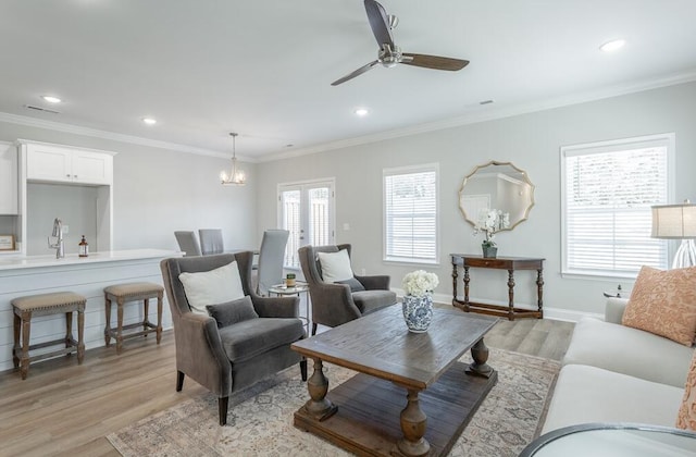 living room with ceiling fan with notable chandelier, light wood-type flooring, and ornamental molding