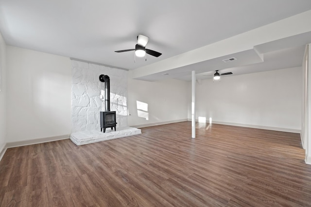 unfurnished living room with dark wood-type flooring, ceiling fan, and a wood stove