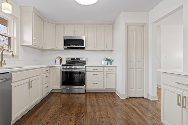 kitchen with pendant lighting, sink, dark wood-type flooring, appliances with stainless steel finishes, and white cabinetry