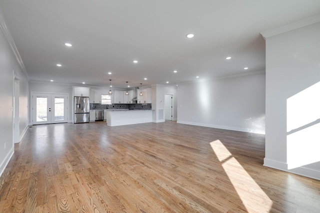 unfurnished living room featuring light wood-type flooring, ornamental molding, and french doors