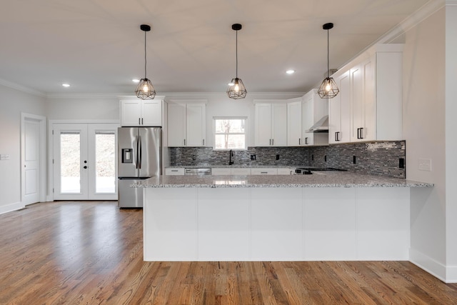 kitchen with kitchen peninsula, decorative backsplash, white cabinetry, light stone countertops, and appliances with stainless steel finishes