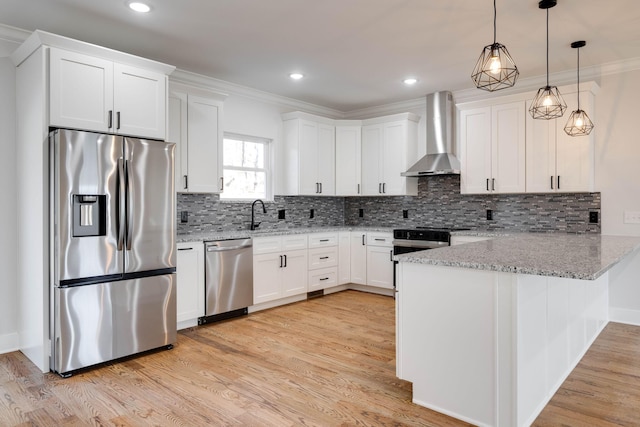 kitchen featuring kitchen peninsula, white cabinetry, hanging light fixtures, appliances with stainless steel finishes, and wall chimney exhaust hood