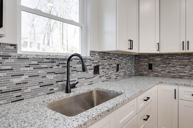 kitchen with white cabinets, light stone countertops, and sink