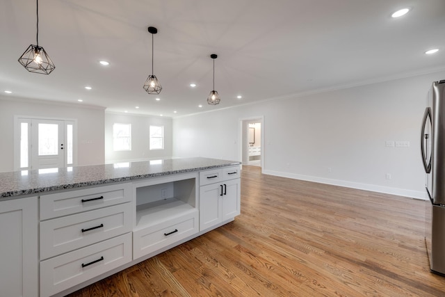 kitchen with stainless steel fridge, decorative light fixtures, light stone countertops, crown molding, and white cabinets