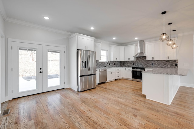 kitchen featuring appliances with stainless steel finishes, white cabinetry, hanging light fixtures, and wall chimney range hood