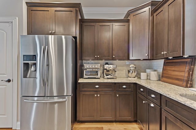 kitchen featuring backsplash, stainless steel refrigerator with ice dispenser, crown molding, dark brown cabinetry, and light stone counters