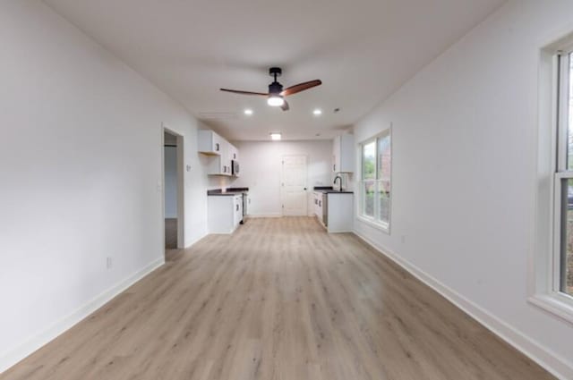 unfurnished living room with sink, ceiling fan, and light wood-type flooring