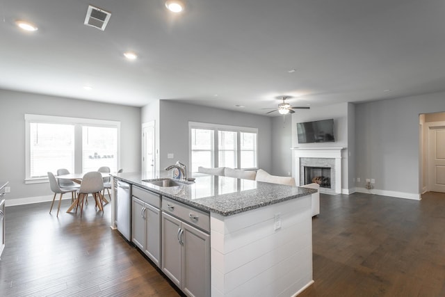 kitchen with dishwasher, a center island with sink, light stone countertops, ceiling fan, and sink