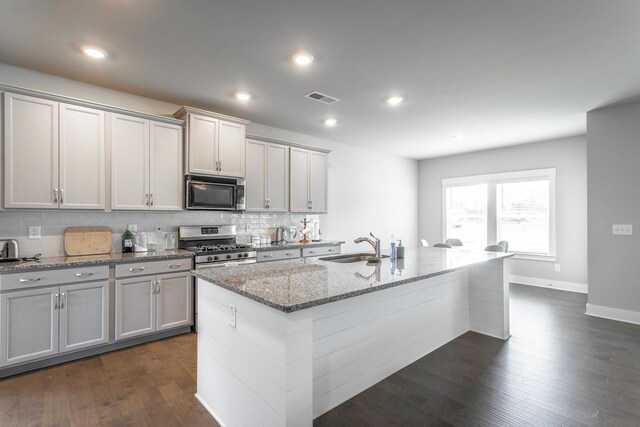 kitchen with sink, an island with sink, light stone counters, and stainless steel gas range oven