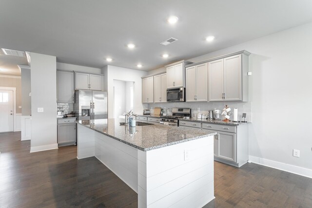 kitchen with light stone countertops, a center island with sink, gray cabinetry, appliances with stainless steel finishes, and sink