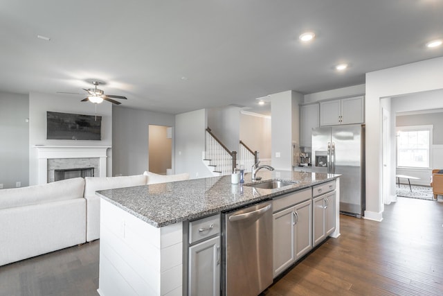 kitchen with a kitchen island with sink, gray cabinets, appliances with stainless steel finishes, stone counters, and sink