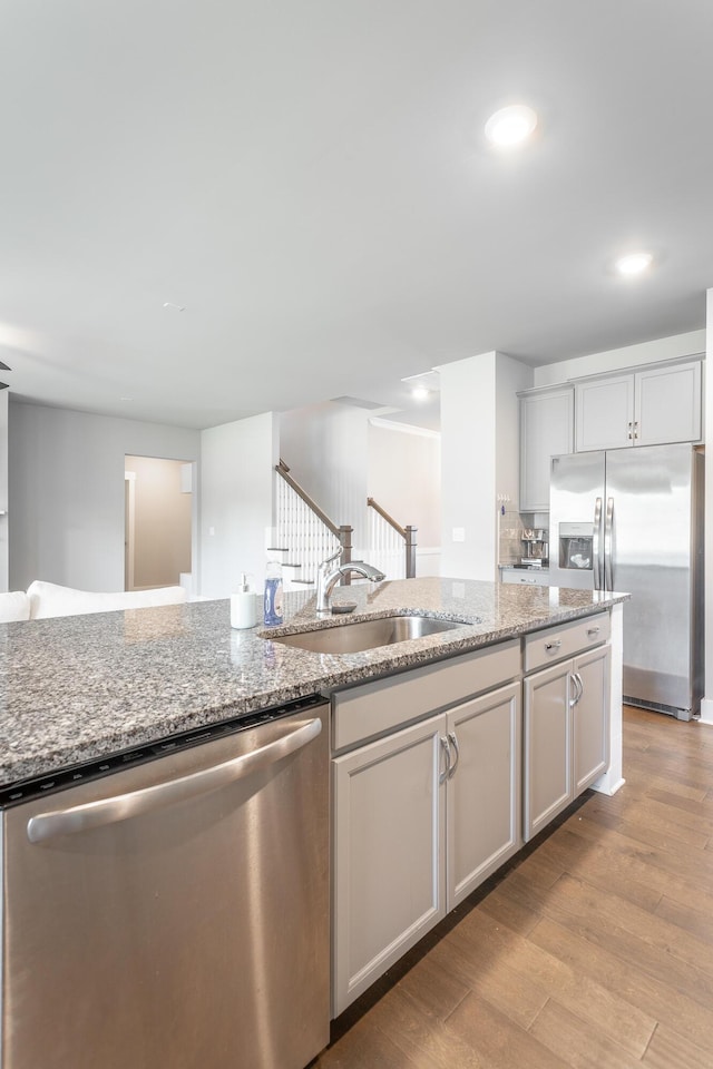 kitchen featuring sink, stainless steel appliances, light wood-type flooring, and light stone counters