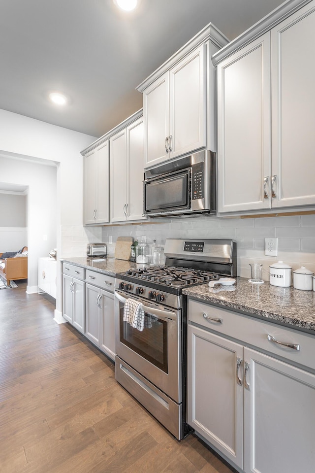 kitchen featuring tasteful backsplash, light hardwood / wood-style floors, stone counters, and appliances with stainless steel finishes