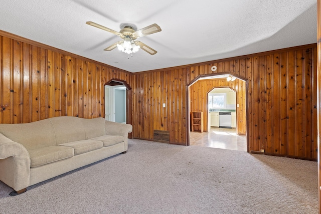 carpeted living room featuring a textured ceiling, ceiling fan, and wooden walls