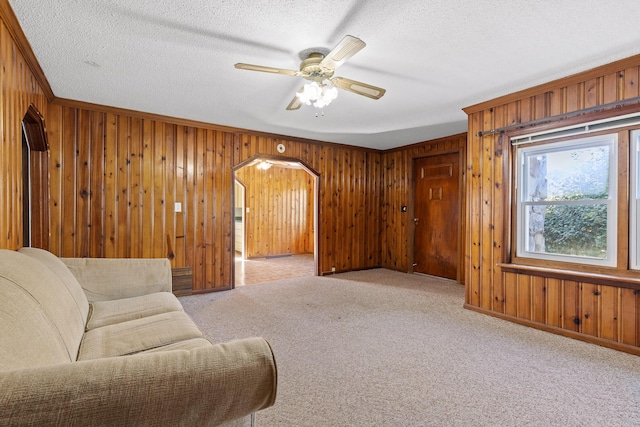 living room featuring light carpet, ceiling fan, a textured ceiling, and wooden walls