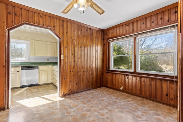 kitchen featuring stainless steel dishwasher, ceiling fan, wooden walls, and ornamental molding