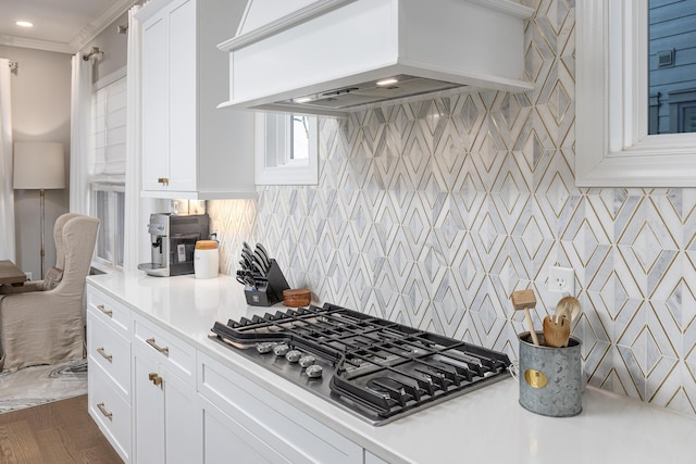 kitchen with white cabinets, light countertops, wall chimney range hood, decorative backsplash, and stainless steel gas stovetop