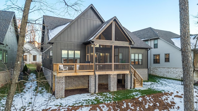 snow covered house with roof with shingles, stairway, board and batten siding, and a sunroom