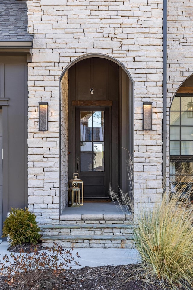 view of exterior entry featuring a shingled roof and brick siding