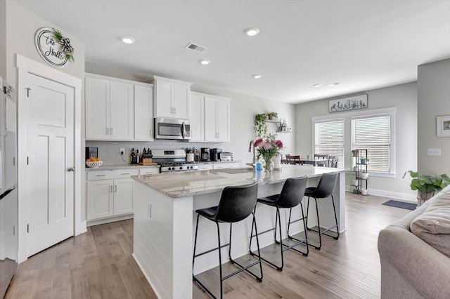 kitchen with white cabinetry, a kitchen island with sink, a breakfast bar area, appliances with stainless steel finishes, and light hardwood / wood-style flooring