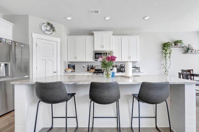 kitchen with light stone counters, a large island, white cabinets, and light hardwood / wood-style flooring