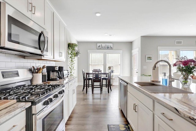 kitchen with appliances with stainless steel finishes, white cabinets, light stone counters, and sink