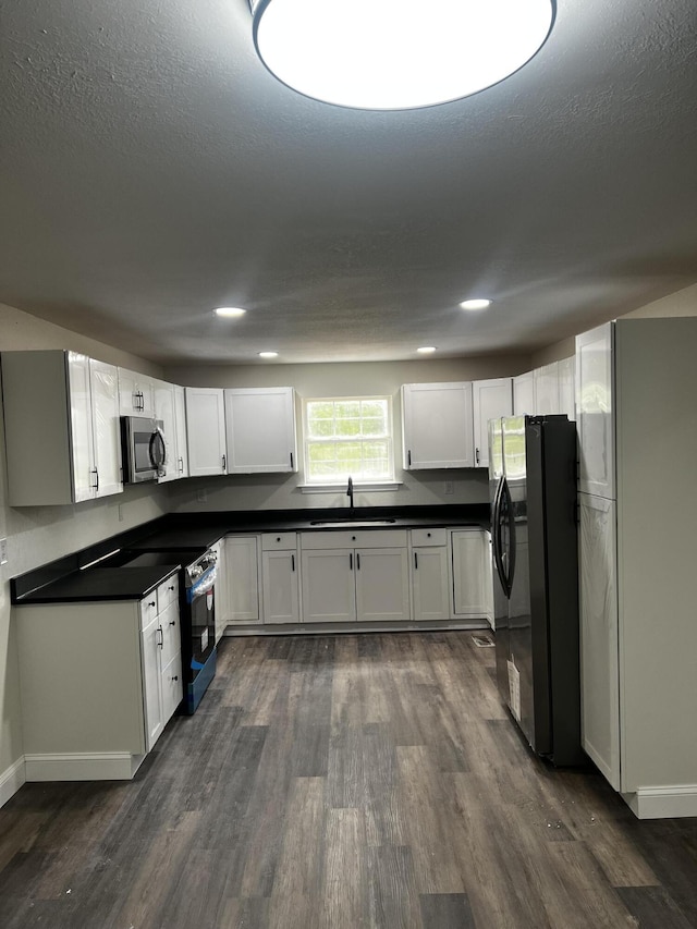 kitchen with appliances with stainless steel finishes, a textured ceiling, dark hardwood / wood-style flooring, white cabinets, and sink